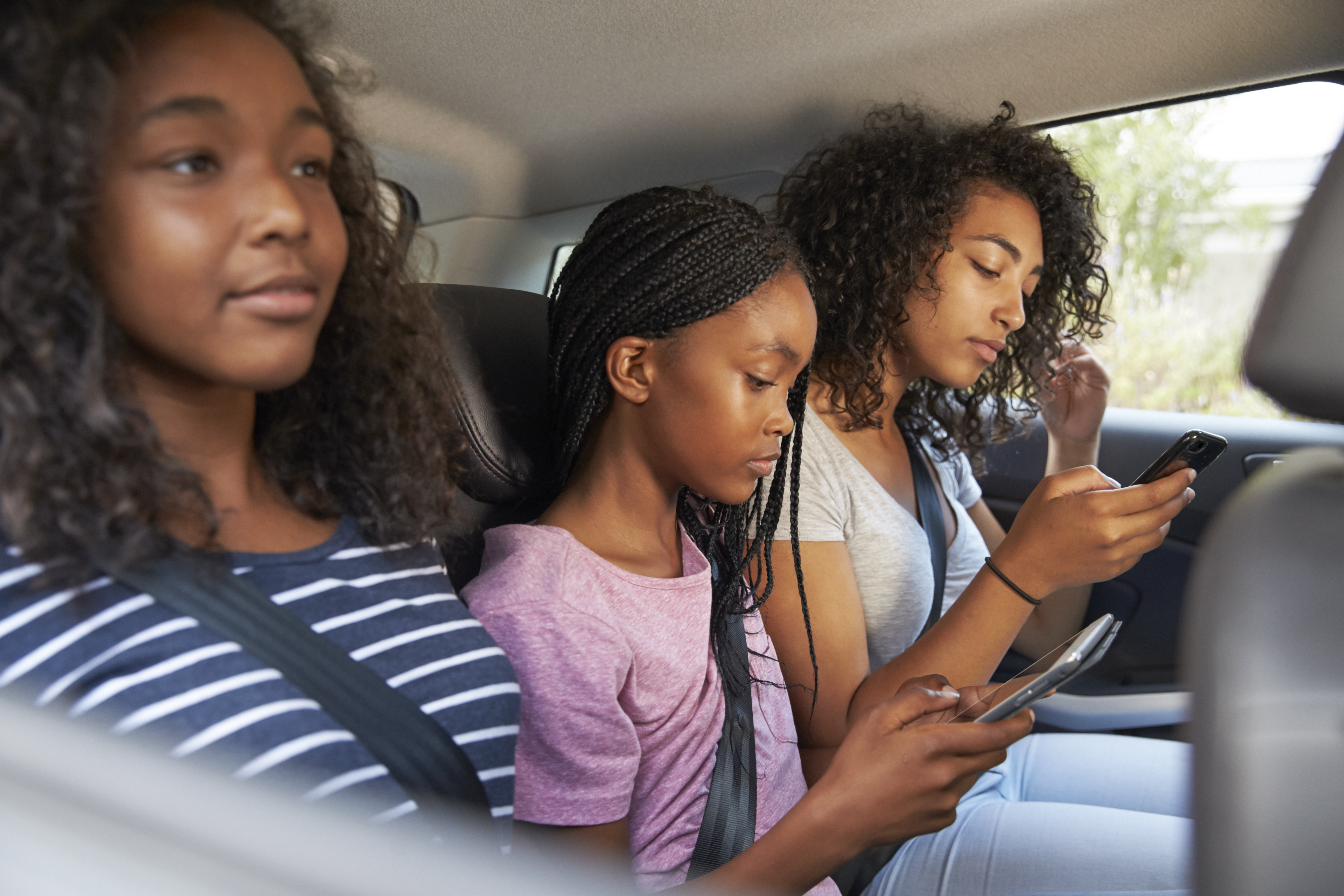 Teenage Children Using Digital Devices On Family Road Trip