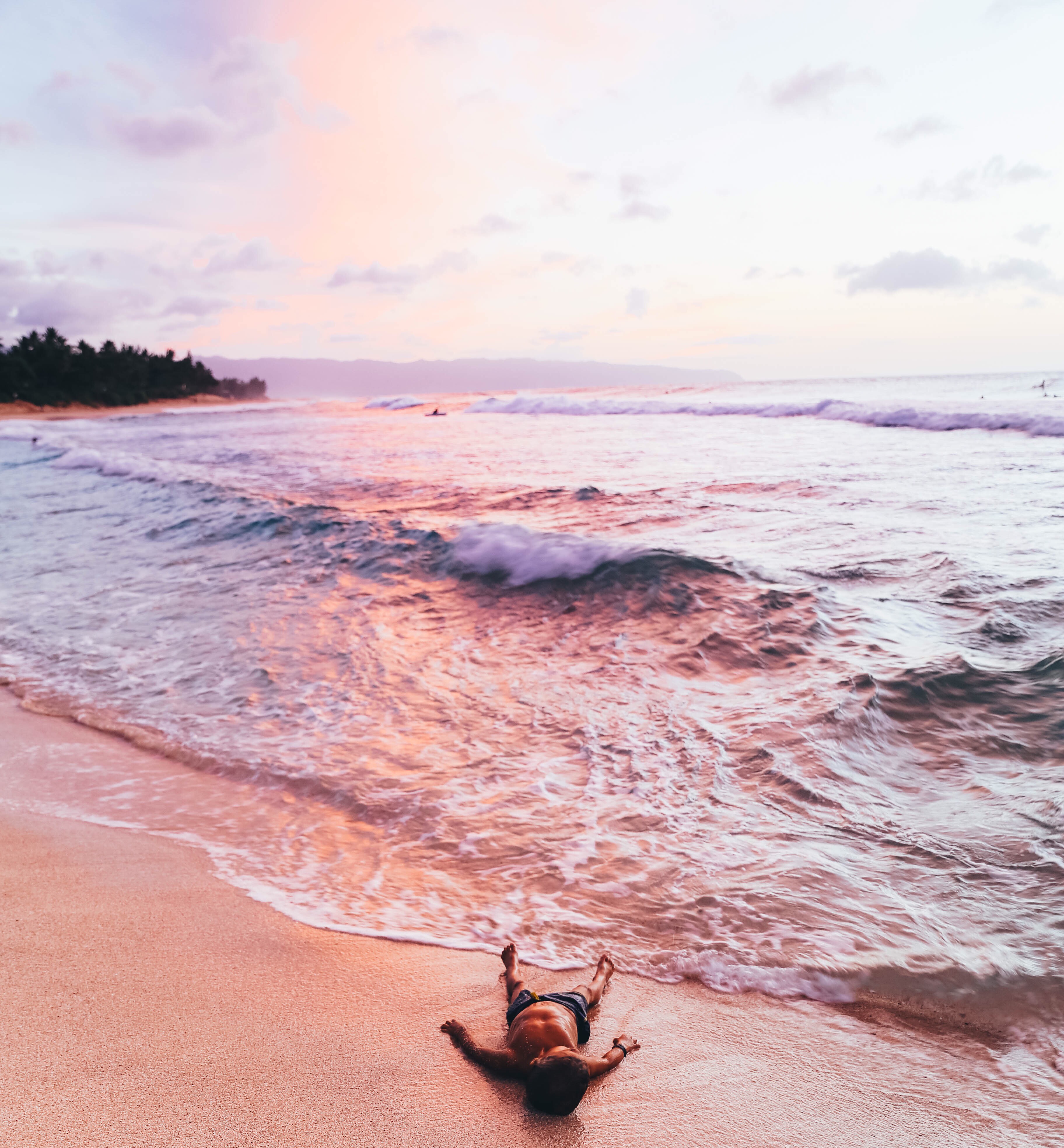 boy laying on beach in front of sunset